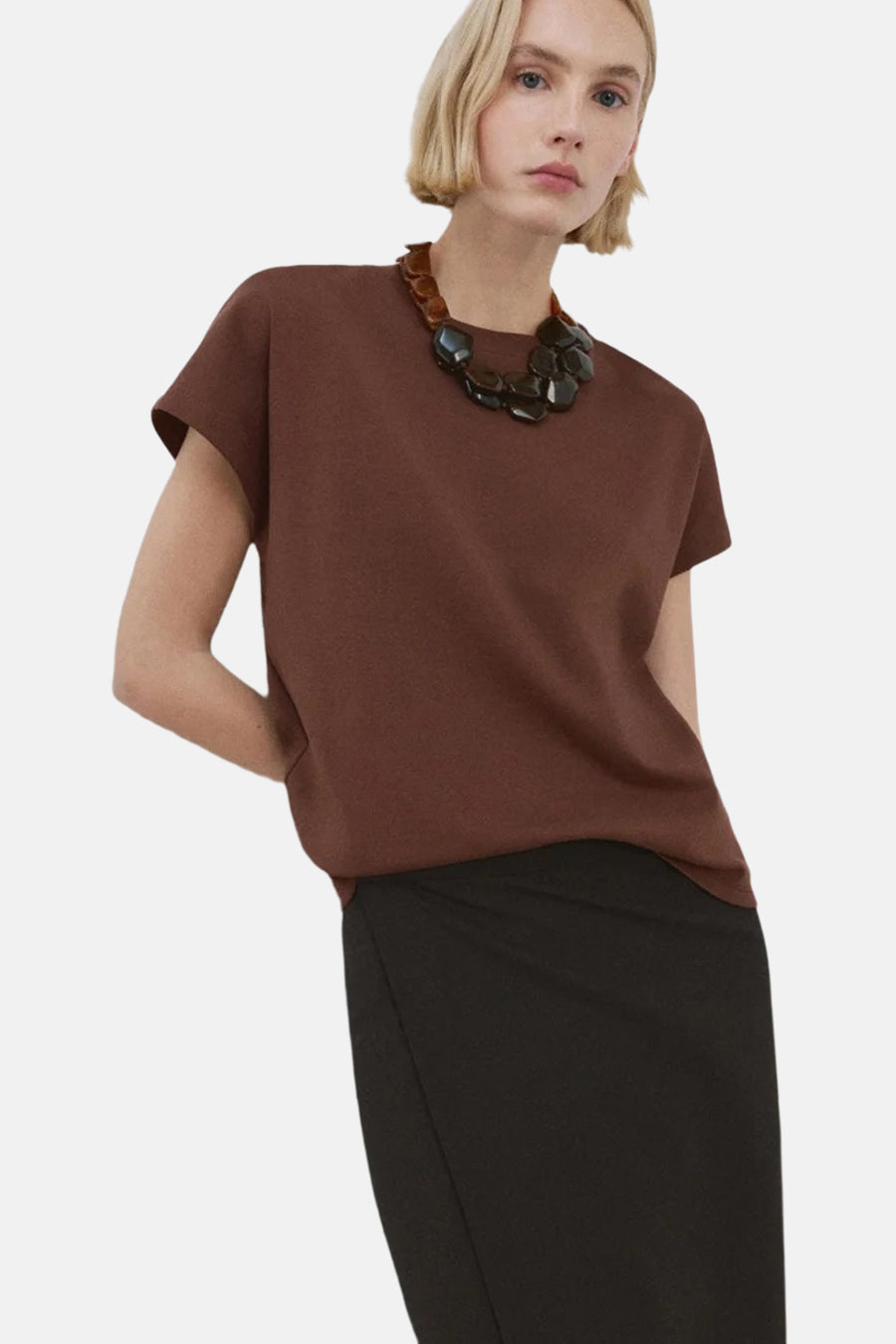 Bruine top van MANGO, gedragen met een zwarte rok en opvallende ketting met bruine en zwarte stenen.