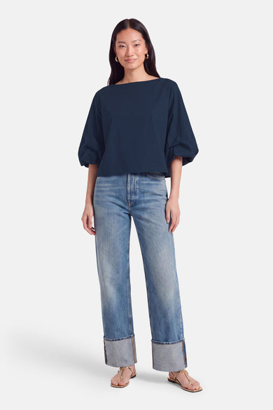 Donkerblauwe blouse met korte mouwen van Terra di Siena, losse pasvorm, gebogen halslijn, gedragen met lichtblauwe jeans en gouden sandalen.