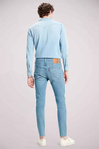 Jean tapered bleu clair de Levi's, avec une étiquette rouge de marque sur la poche arrière et un t-shirt bleu clair décontracté.