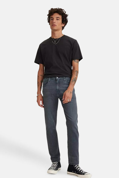 Jean tapered en denim noir de Levi's®, associé à un T-shirt noir, des sneakers hautes et des chaînes d'argent.