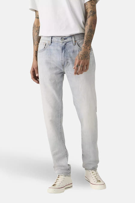 Jeans tapered van lichtblauw denim van Levi's®, met zichtbare tattoos op de armen en witte sneakers.
