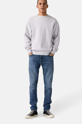 Blauwe tapered jeans van Levi's, gecombineerd met een grijze sweater en zwarte sneakers.