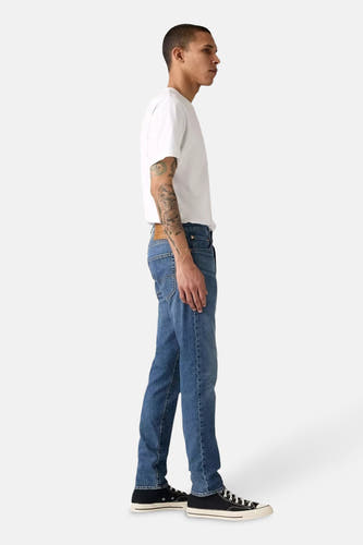 Tapered jeans in middenblauw denim van Levi's, gedragen met een wit T-shirt en zwarte sneakers, zijaanzicht.