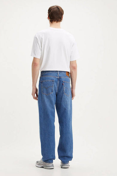 Jean large de denim bleu moyen de Levi's, vu de derrière, associé à un T-shirt blanc et des baskets grises.