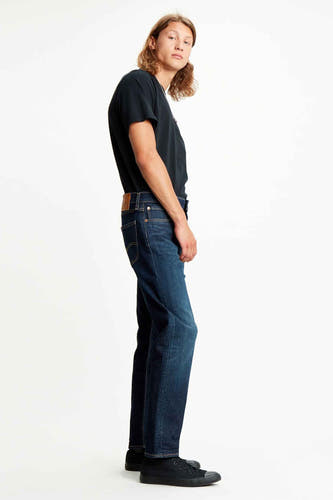 Donkerblauwe tapered jeans van Levi's, gedragen met een zwart T-shirt en zwarte sneakers, in zij aanzicht.
