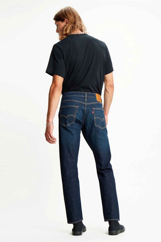 Donkerblauwe tapered jeans van Levi's, gezien van achteren, met een bruin leren patch en rode merklabel.