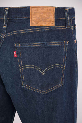 Donkerblauwe tapered jeans van Levi's, met een bruin leren merklabel op de achterkant en rode merklabel op de achterzak.
