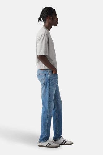Tapered jeans van Levi's®, in een medium blauwe denimkleur, gecombineerd met een grijs T-shirt en witte sneakers.
