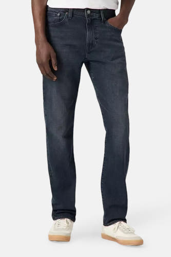 Donkergrijze tapered jeans van Levi's, met een hand in de zak en gecombineerd met crèmekleurige sneakers.
