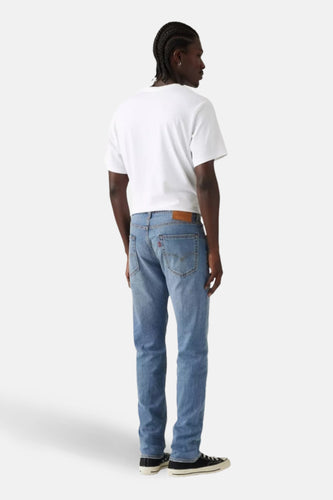 Lichtblauwe tapered jeans van Levi's, met bruin leren patch en gedragen met een wit T-shirt en zwarte sneakers.