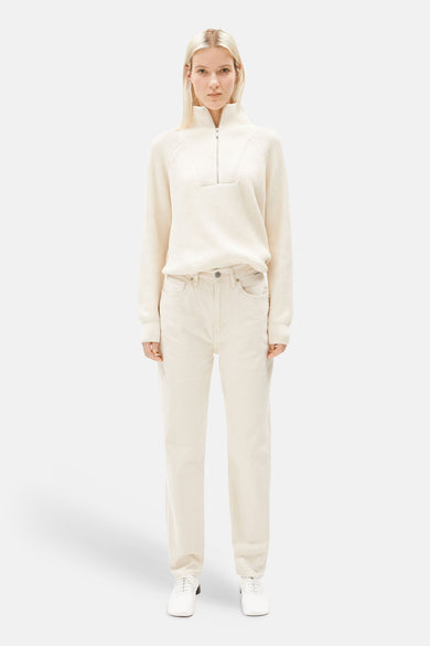 Off white mom jeans van ARMED ANGELS, gedragen met een crèmekleurige trui met ritssluiting en witte schoenen.