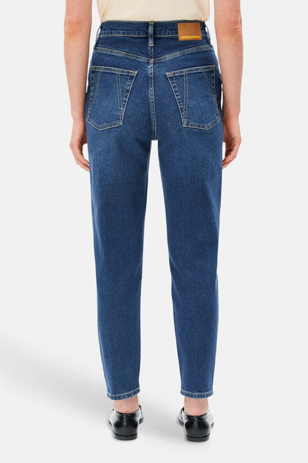 Donkerblauwe mom jeans van Armed Angels, achterzijde met klassieke zakken en bruin label, gedragen met crèmekleurig topje en zwarte schoenen.