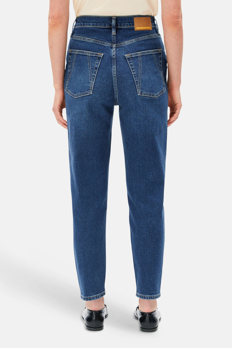 Donkerblauwe mom jeans van Armed Angels, achterzijde met klassieke zakken en bruin label, gedragen met crèmekleurig topje en zwarte schoenen.