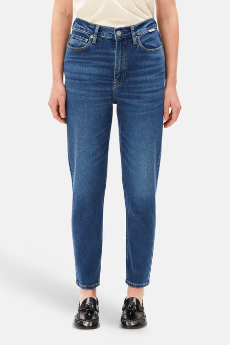 Donkerblauwe mom jeans van Armed Angels, front view, met lichte was, hoge taille en slanke pasvorm, gedragen met crèmekleurig topje en zwarte loafers.