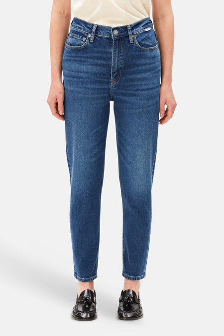 Donkerblauwe mom jeans van Armed Angels, front view, met lichte was, hoge taille en slanke pasvorm, gedragen met crèmekleurig topje en zwarte loafers.