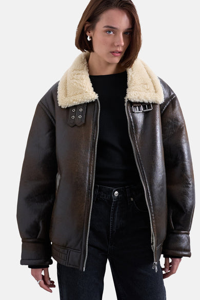Bruine korte jas van TOPSHOP, met een witte, wollen kraag en een zilveren ritssluiting, gedragen over een zwarte top en jeans.
