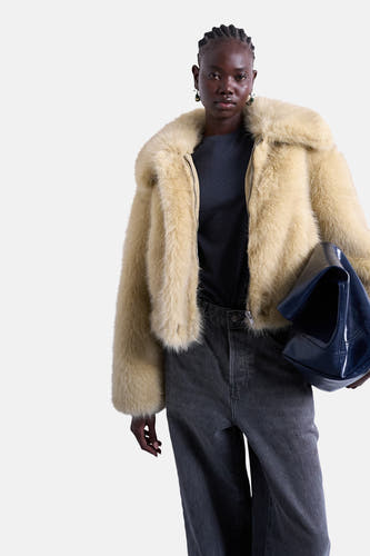 Gele korte jas van TOPSHOP, met een harige textuur, gedragen over een donker shirt en grijze jeans.