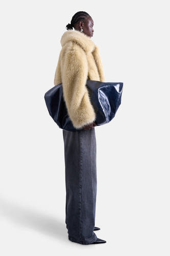 Gele korte jas van TOPSHOP, gedragen met een grote blauwe lakleren tas en wijde grijze jeans, zijdelings gefotografeerd.
