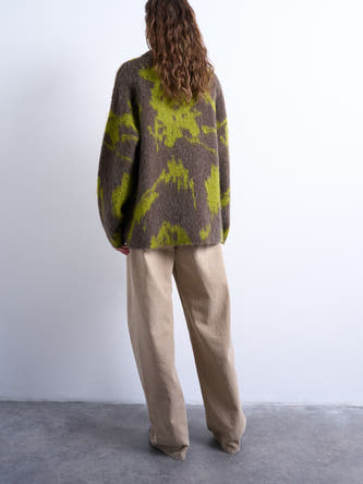 Multikleurige trui met ronde hals van TOPSHOP, met een abstract bruin en groen patroon, gedragen met beige broek.
