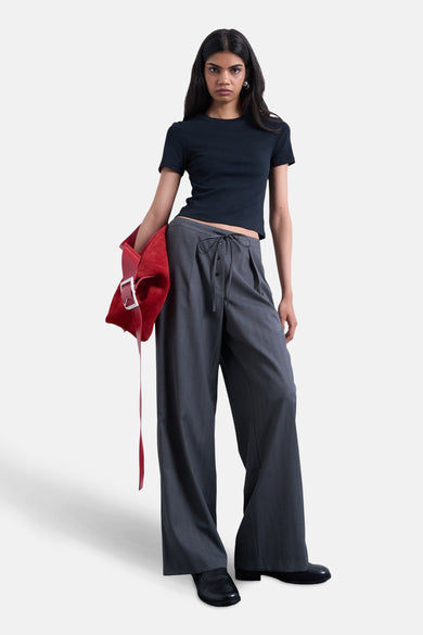 Grijze broek van TOPSHOP, met wijde pijpen en striksluiting, gecombineerd met een donkerblauw shirt en een rode handtas.