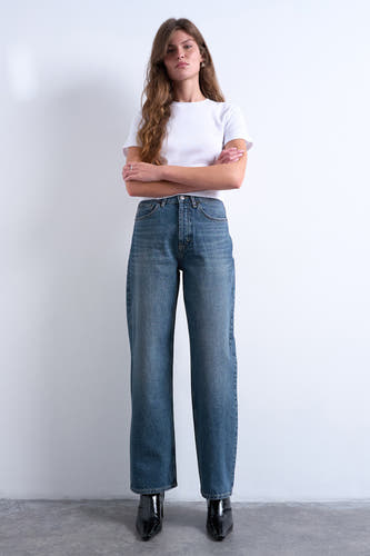 Straight jeans mid blue denim van TOPSHOP, met een witte T-shirt en zwarte laarzen.
