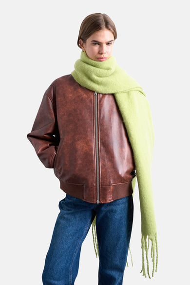 Manteau d'hiver vert de TOPSHOP, avec des franges, associé à une chemise rose et un pantalon en cuir marron avec des bottes.