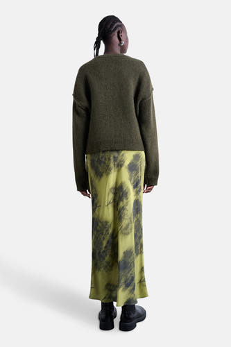 Long manteau vert de TOPSHOP, avec des taches sombres abstraites et porté avec un pull vert.