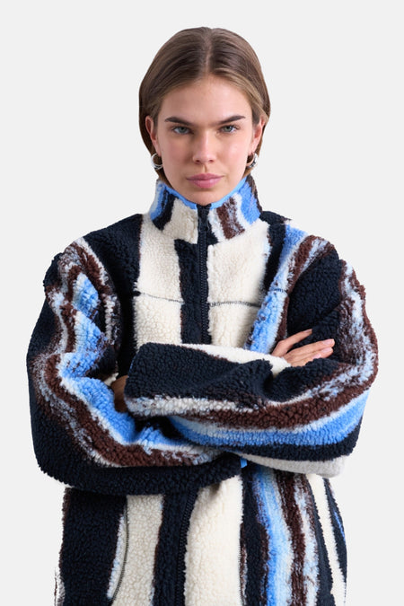 Een vrouw met gekruiste armen die een gestreepte fleece vest draagt.