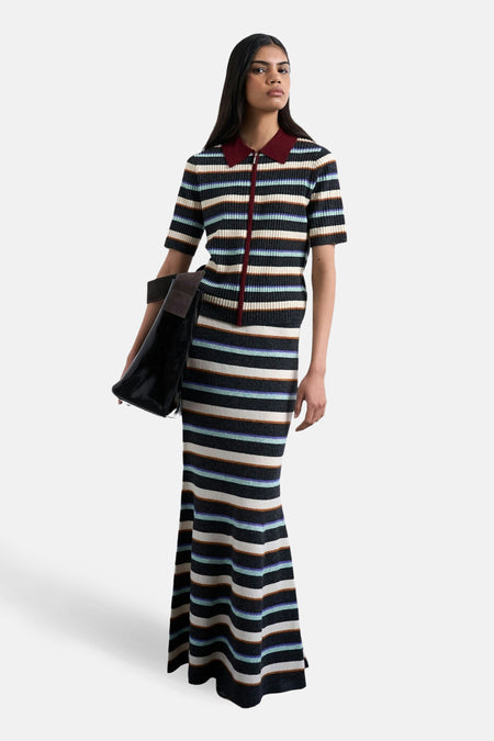 Vrouw in gestreepte polo en lange rok met handtas.