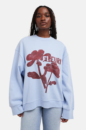 Blauwe sweater met ronde hals van TOPSHOP, met rode bloemenprint en de tekst 'FLEURI'.
