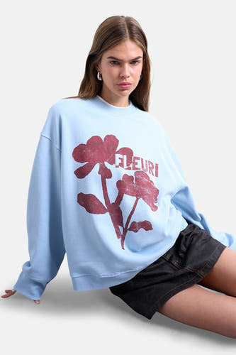 Blauwe sweater van TOPSHOP, met rode bloemenprint en de tekst 'FLEURI', gedragen met een zwarte rok.
