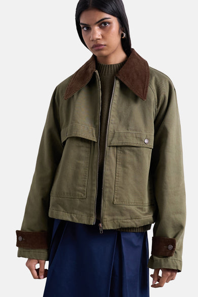 Manteau court vert de TOPSHOP, avec un col et des manchettes marrons, porté avec une chemise verte et une jupe bleue.