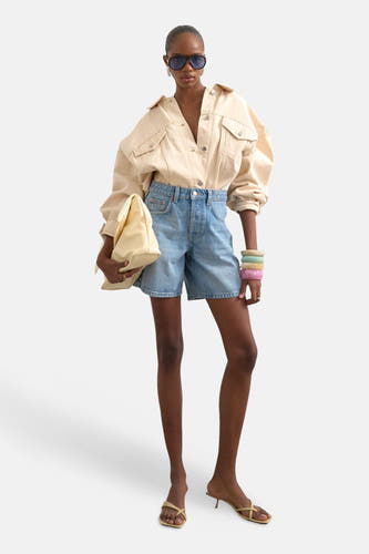 Lichtblauwe denim shorts van TOPSHOP, hoge taille, rechte pasvorm, met beige overhemd en zonnebril, front view