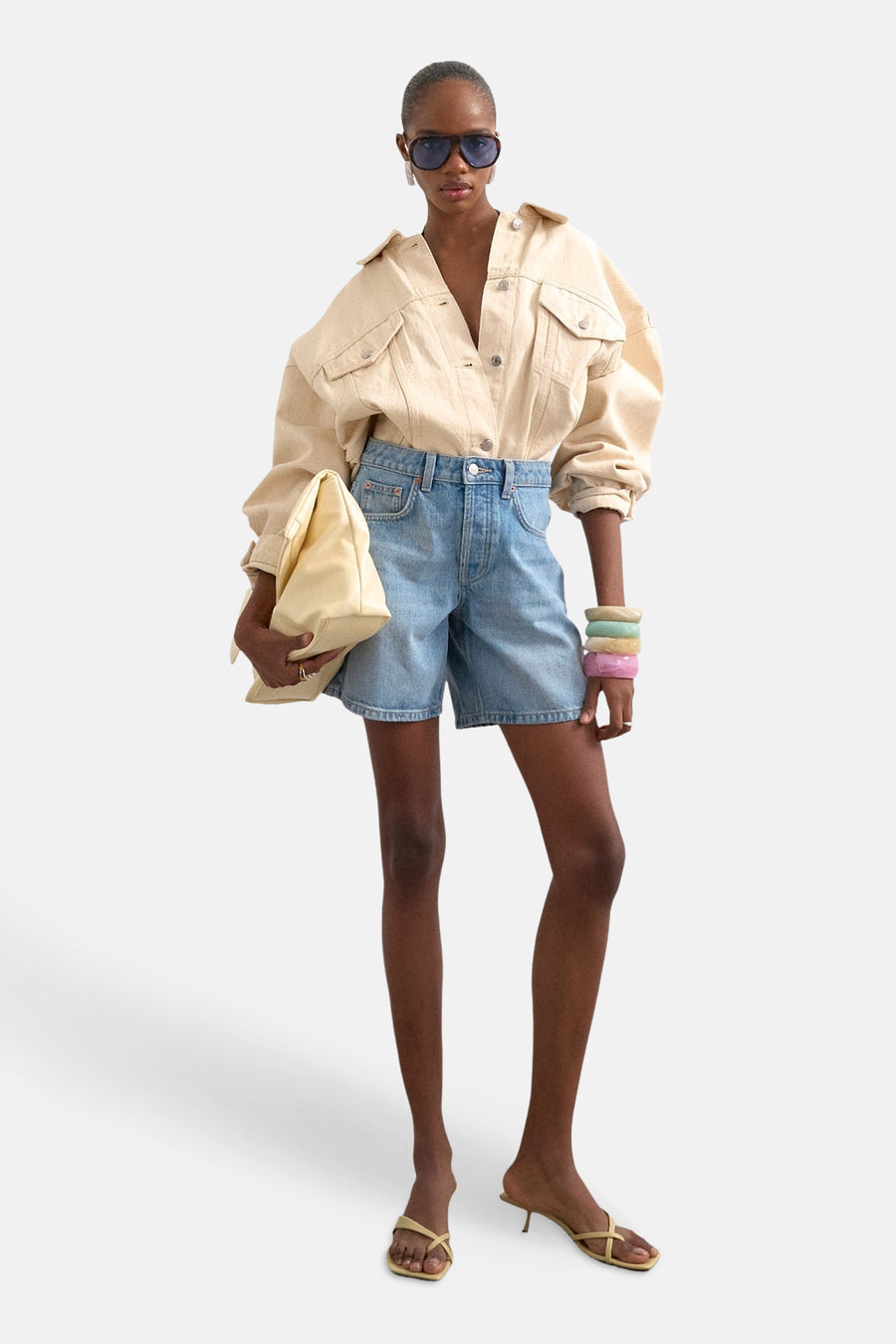 Lichtblauwe denim shorts van TOPSHOP, hoge taille, rechte pasvorm, met beige overhemd en zonnebril, front view