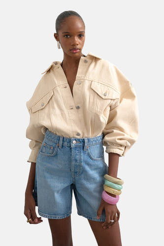 Lichtblauwe denim shorts van TOPSHOP, hoge taille, rechte pasvorm, met zakken, gedragen met een beige overhemd en kleurrijke armbanden.
