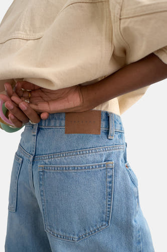 Lichtblauwe denim shorts van TOPSHOP, achterzijde met bruin label, zakken en beige shirt, close-up.