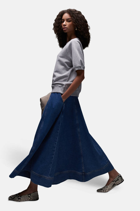 Jupe longue en denim bleu moyen de TOPSHOP, évasée avec surpiqûres apparentes, portée avec un pull gris et des ballerines à imprimé serpent.