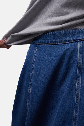 Mid-blauwe denim A-lijn rok van TOPSHOP met verticale naden, gedragen door een persoon in een grijs sweatshirt.