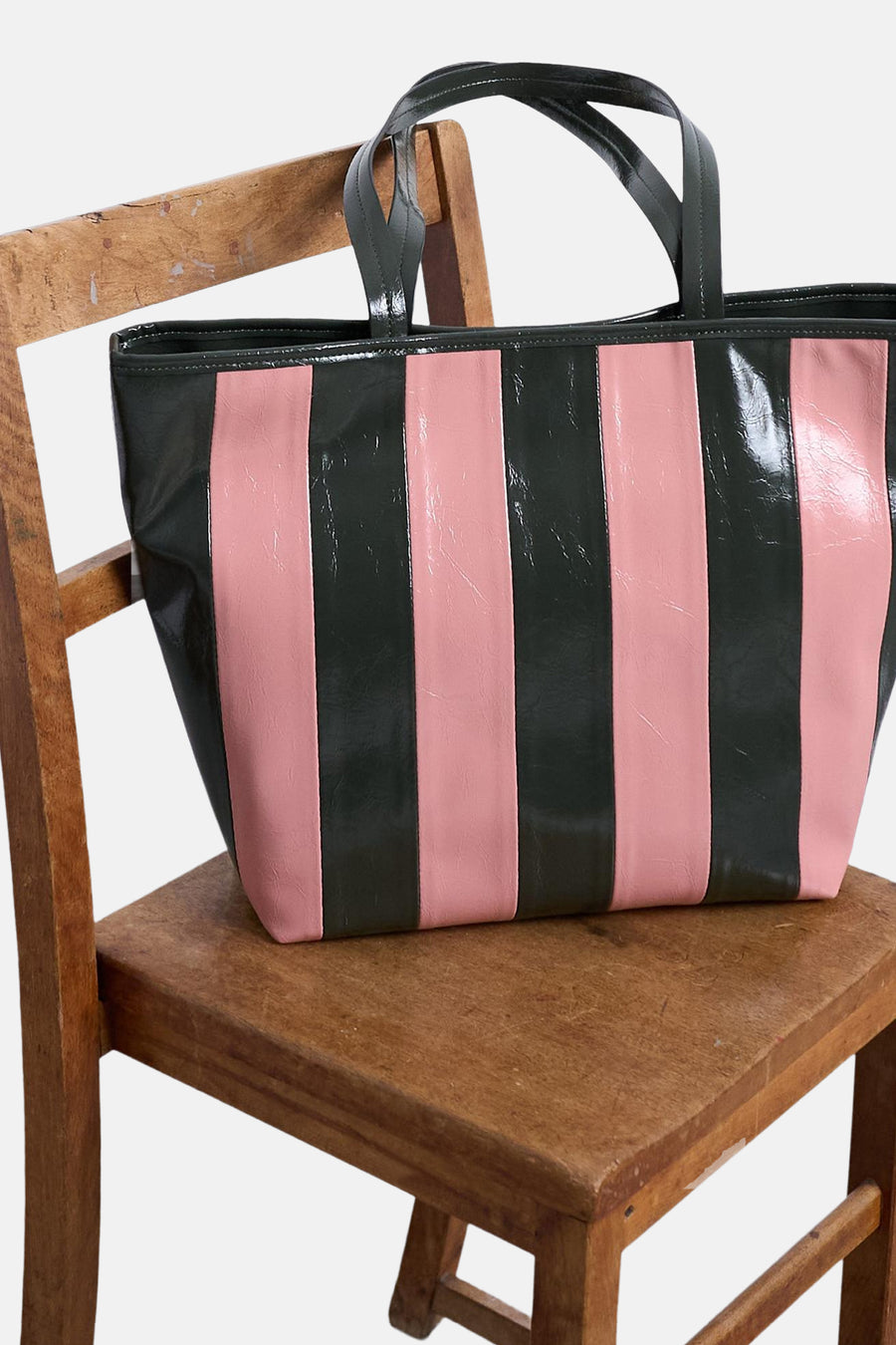 Sac à bandoulière rose de TOPSHOP avec des rayures noires verticales, posé sur une chaise en bois.