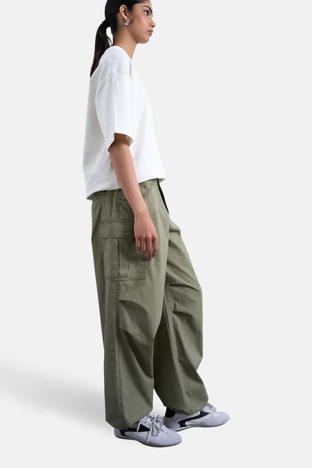 Groene cargobroek van TOPSHOP, met steekzakken en gedragen met een wit t-shirt en grijze sneakers, in zij-aanzicht.
