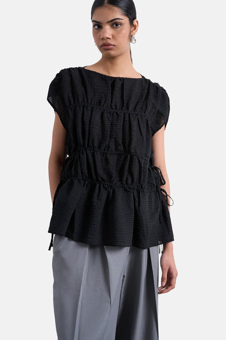 T-shirt noir de TOPSHOP, avec une texture plissée et des détails de nœud sur le côté, combiné avec un pantalon gris.