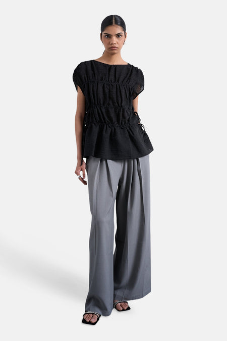 T-shirt noir de TOPSHOP, avec détail plissé et manches courtes, combiné avec un pantalon gris ample et des sandales.