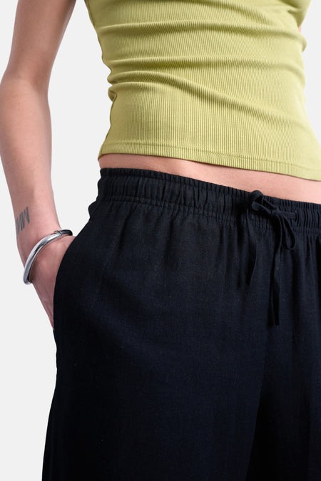 Zwarte broek van TOPSHOP, met een elastische tailleband en een koord, gedragen met een zilveren armband.
