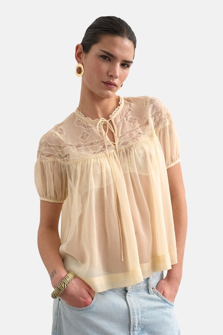 Blouse écru à manches courtes de TOPSHOP, avec détails en dentelle et associée à un jean et un bracelet voyant.