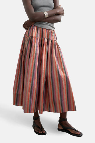 Multikleurige rok van TOPSHOP, met gestreepte patronen, gecombineerd met een grijze top en zwarte sandalen.
