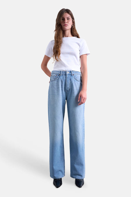 Jean droit en denim bleu moyen de TOPSHOP, taille haute et jambes larges, porté par un mannequin avec un t-shirt blanc et des chaussures noires.