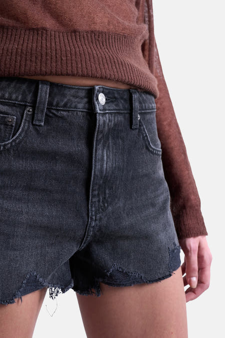 Zwarte denim short van TOPSHOP, met gerafelde randen en een bruine trui gedeeltelijk zichtbaar.
