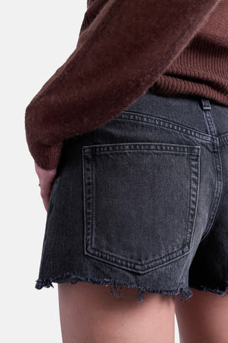 Short en jean noir de TOPSHOP, avec ourlet effiloché et un pull en tricot marron en arrière-plan.