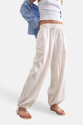 Pantalon blanc ample de TOPSHOP avec cordon de serrage à la taille et ourlets élastiques, porté avec un débardeur blanc et des tongs.