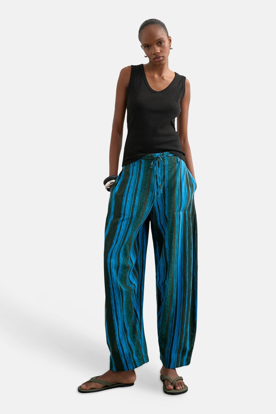 Blauwe broek van TOPSHOP, verticaal gestreept in blauw en donkergroen, met trekkoord en wijde pijpen, gedragen met een zwarte top en teenslippers.